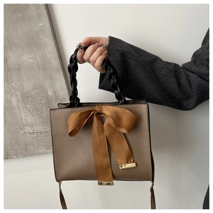 Détail d'un sac à main en cuir marron avec un grand nœud en satin et une poignée tressée