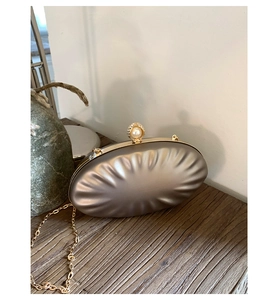 Close-up of champagne gold clutch with pleated texture, pearl clasp and metal chain strap