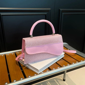 Pink crossbody bag with wavy flap and round handle on a wooden bench
