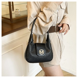 Detail shot of black woven handbag with gold M logo on a model in cream studio