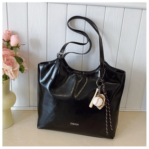 Detail of black faux leather tote bag with FASHION text and baseball charm accessory