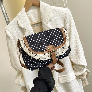 Retro polka dot crossbody bag with white lace trim and leather strap held by hand