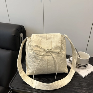 Creamy nylon tote bag with bow detail on a black wooden tray for daily commuting
