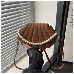 Detail of a brown suede shell-shaped bag with a pearl handle and gold metallic accents