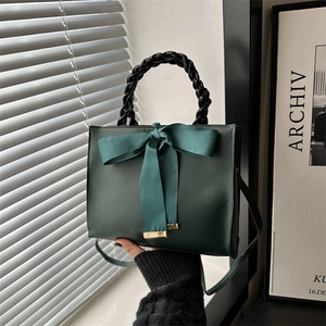 Sac bandoulière vert foncé avec nœud et poignée tissée dans un décor minimaliste
