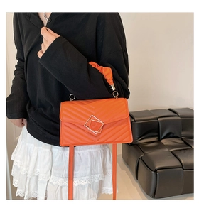 Close-up of orange quilted crossbody bag with V-shaped stitching and ruffle handle