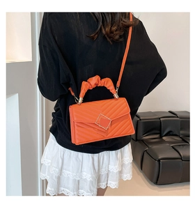 Detail of orange quilted handbag with ruched handle and metal clasp on shoulder