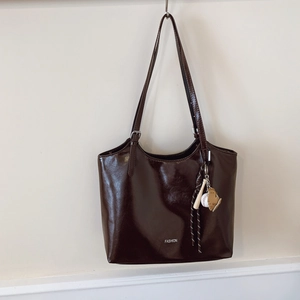 Brown oil wax leather tote bag with FASHION text and baseball charm hanging on a wall