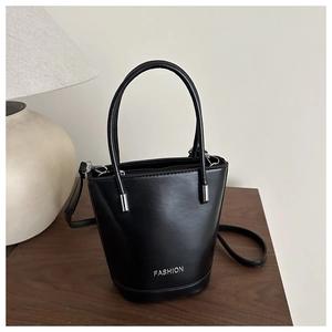 Detail of a structured black bucket bag with FASHION lettering on a wood surface
