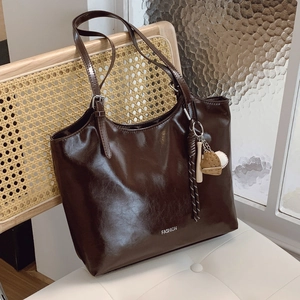 Large dark brown patent leather tote bag with FASHION text on a rattan chair