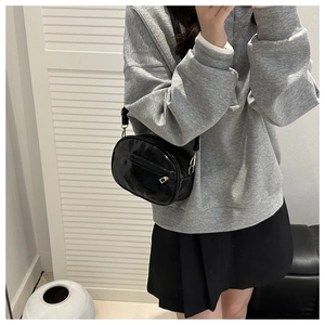 Detail of a black glossy PU leather crossbody bag with golden hardware and outer pocket