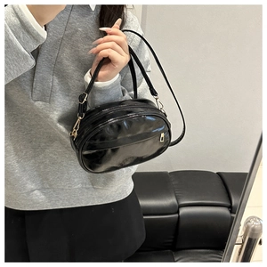Detail of black glossy PU leather crossbody bag with gold zipper and adjustable strap