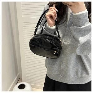 Detail of glossy black patent leather shell bag with adjustable golden metal buckle