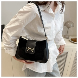 Detail of black crossbody bag with matte拼接 texture and metallic bow buckle on flap