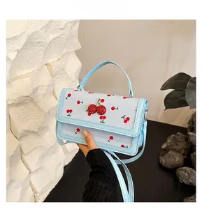 Dettaglio della borsa azzurra con motivi a ciliegia e chiusura decorativa a ciliegia