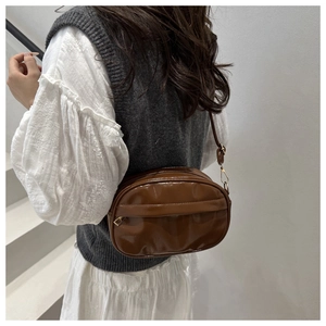 Détail d'un sac bandoulière ovale marron brillant avec finition laquée et fermeture éclair