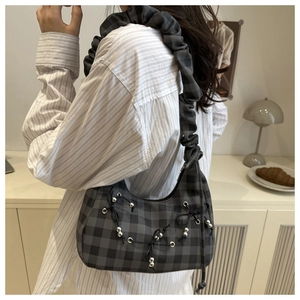 Detail der karierten Falten-Cloud-Tasche mit Schleifen und Silberperlen an einem Model