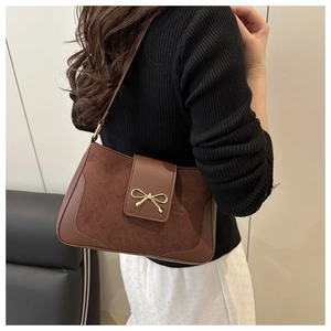 Detail of retro shoulder bag featuring dark brown suede patchwork and gold bow buckle