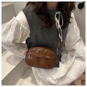 Detail of a brown glossy shell crossbody bag with adjustable strap on a model