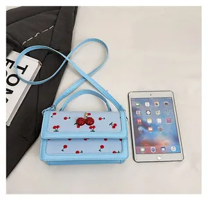 Vista piatta della piccola borsa azzurra con stampa ciliegie accanto a un tablet