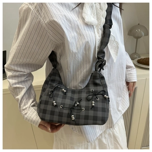 Detail of gingham shoulder bag with bow accents and pleated strap on a model