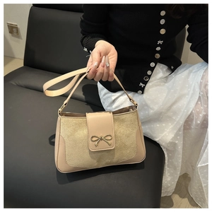 Detail of beige shoulder bag with gold bow clasp and mixed leather texture contrast