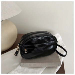 Détail d'un sac bandoulière en cuir verni noir avec fermeture éclair dorée et style moderne