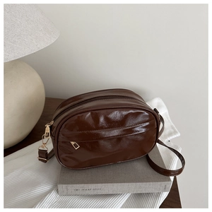Détail du sac bandoulière marron foncé brillant avec double zip sur des livres de mode
