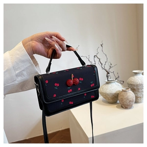 Detail of sequin cherry embellishment on black canvas handbag with leather trim