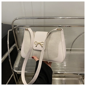 Close-up of a white shoulder bag featuring a golden bow buckle and mixed textures