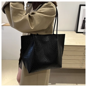 Black woven tote bag styled with a khaki trench coat in a cozy indoor lifestyle setting