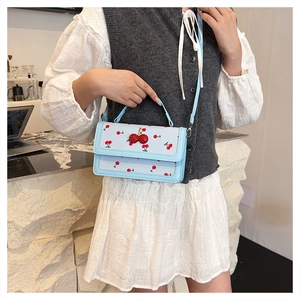 Detail of light blue cherry print handbag with a 3D cherry pendant and a top handle