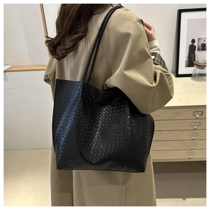 Detail of a large black woven texture tote bag worn on shoulder in a lifestyle setting