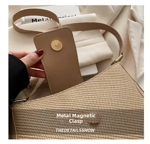 Detail of the golden magnetic closure on the woven beige shoulder bag with a hand opening it