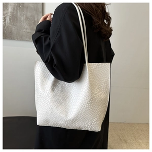 Detailed side view of white woven texture tote bag worn on shoulder by a model