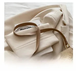 Detail of light brown woven texture bag with metal bow buckle on beige blazer