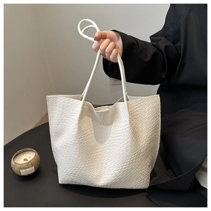 Close-up of white crocodile pattern tote bag with slender double handles on black backdrop