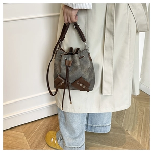 Detail view of a gray canvas bucket bag with brown leather trim and metal grommet pockets