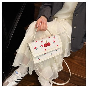 Detail shot of white leather crossbody bag with red cherry patterns and 3D cherry accents