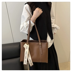 Dettaglio borsa tote marrone con nastro bianco 'FASHION' e tracolla regolabile
