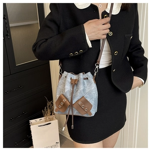 Detail of blue denim bucket bag featuring brown leather drawstring and metal eyelets