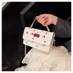 Detail of white fashion handbag with cherry prints and 3D cherry buckle detail