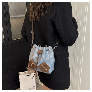 Detail of blue denim bucket bag with drawstring closure and brown faux leather pockets