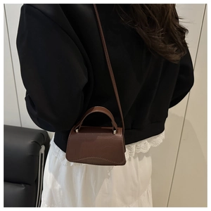 Détail du mini sac bandoulière marron foncé effet crocodile porté par un mannequin