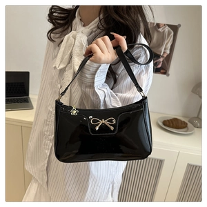 Detail of black glossy patent leather shoulder bag with gold metal bow and flower charm