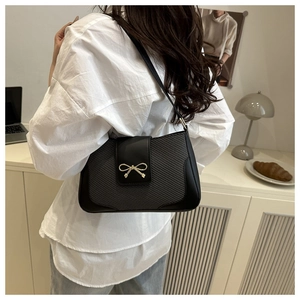 Detail of black leather underarm bag with gold bow clasp and woven texture panel