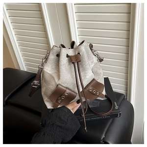 Detail of canvas bucket bag with brown leather trim and drawstring closure on a books scene