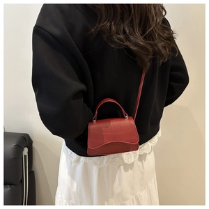 Detail of red crocodile textured mini crossbody bag shown on a model's shoulder