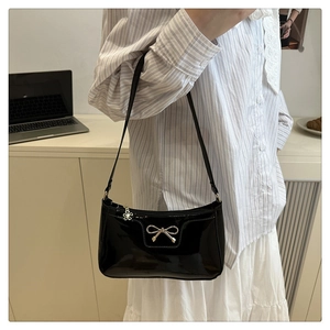 Detail of black patent leather underarm bag with gold bow ornament and floral charm