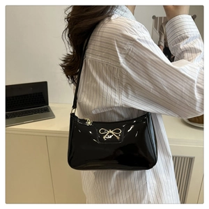 Close-up of black patent leather baguette bag with golden bow and floral pendant